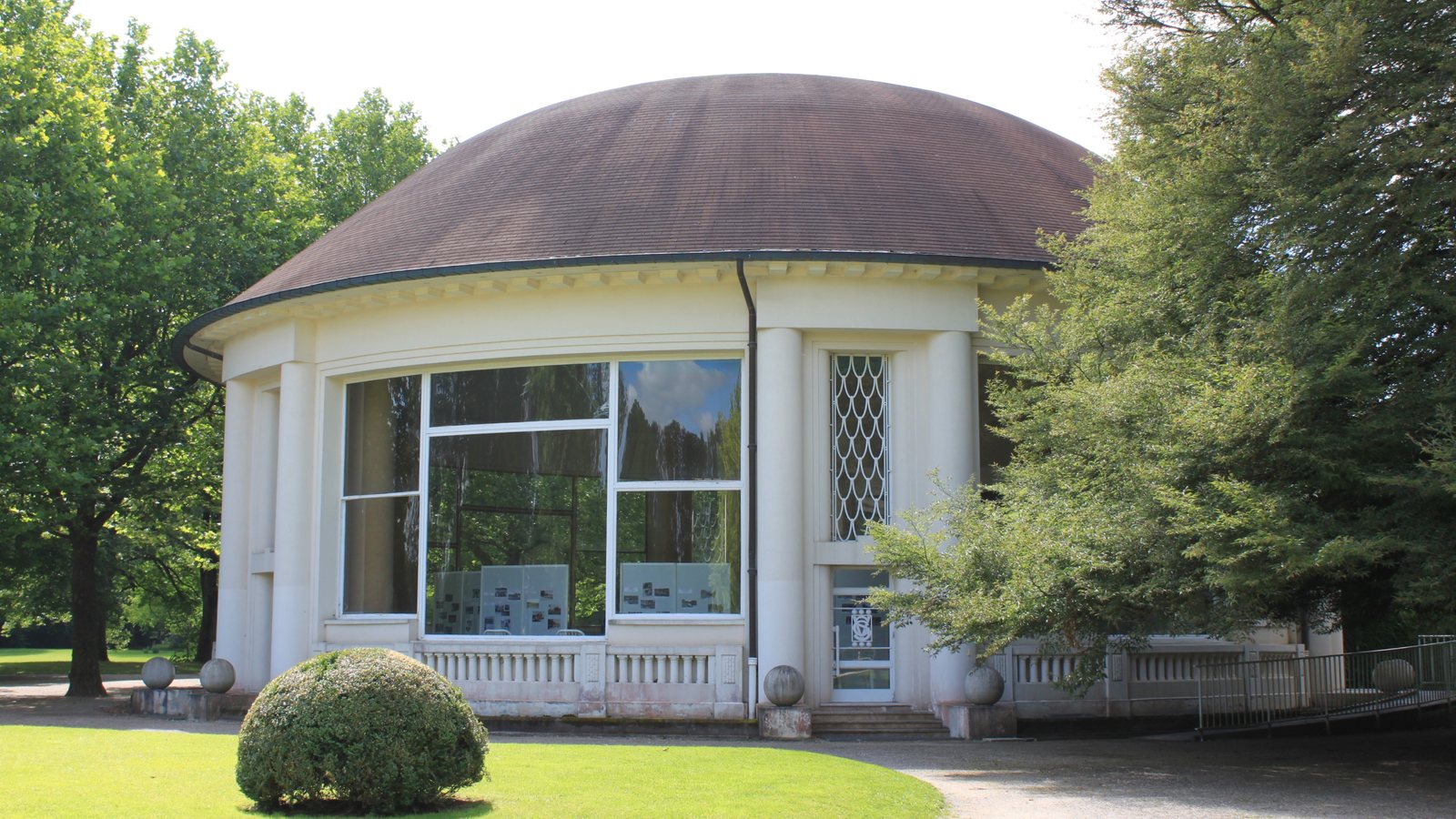 Un pavillon à coupole et grandes baies vitrées dans le parc thermal de Vittel, entouré d'arbres